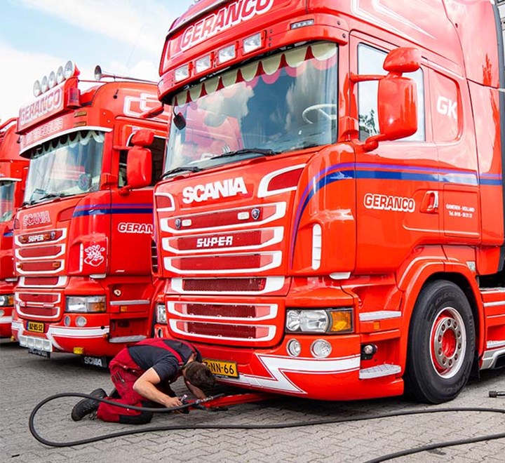 Medewerker checkt iets aan de onderkant van een rode vrachtwagen